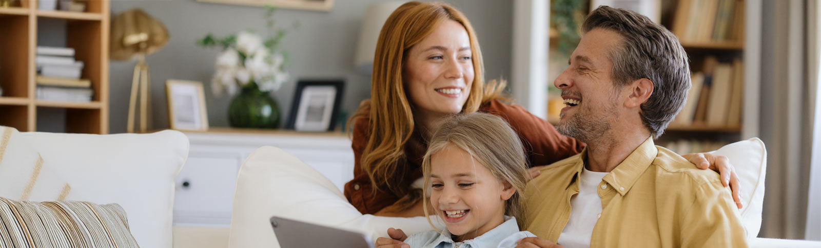 Immagine di una famiglia sorridente: a sinistra un uomo sorride a una signora sulla destra e in mezzo a loro una bambina che guarda un tablet